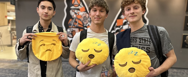 Three students holding emoji pillows